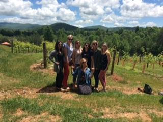 Group of people standing in front of a vineyard and smiling